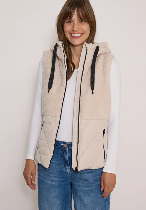 Frau trägt beige Weste mit Kapuze über weißem Shirt und Jeans