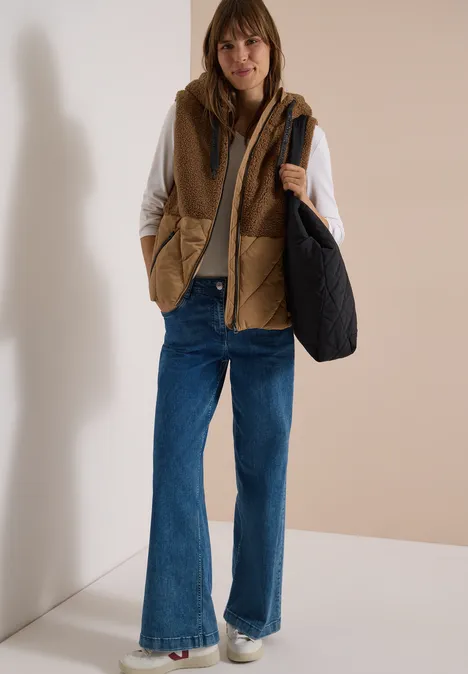 Teddy-Weste mit Steppteil und Zipper dark toffee brown Frau mit brauner gesteppter Weste, weißem Oberteil, weiten Jeans, Sneakern und schwarzer Tasche.
