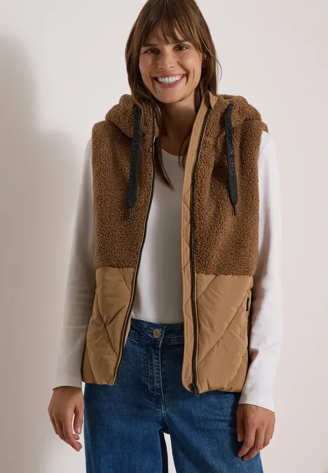 Teddy-Weste mit Steppteil und Zipper dark toffee brown Lächelnde Frau in weißem Langarmshirt, blauen Jeans und brauner, gesteppter Teddyweste mit Kapuze.