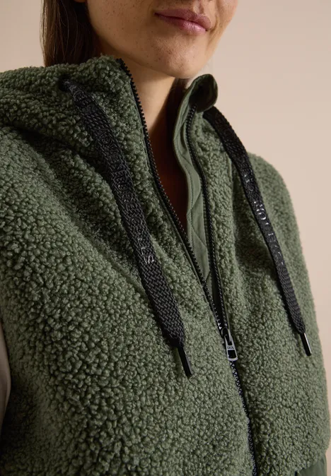 Teddy-Weste mit Steppteil und Zipper shadow khaki Nahe Aufnahme einer Person in einem olivgrünen Teddy-Fleece-Hoodie mit Reißverschluss und schwarzen Kordeln.