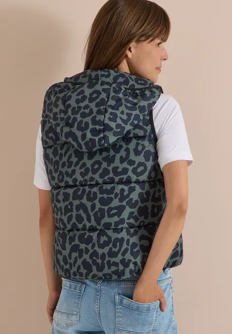 Steppweste mit Kapuze und Taschen dried olive green Frau von hinten im weißen T-Shirt und ärmelloser Kapuzenweste mit Leopardenmuster, Hand in Jeans-Tasche.