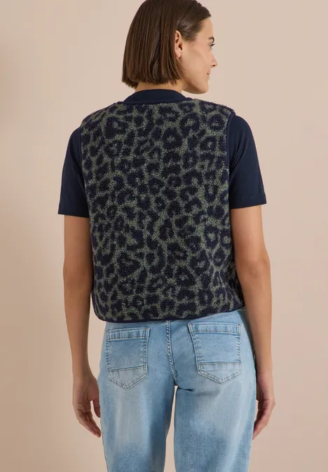 Teddy-Weste mit Softshelldetails und Leo-Muster dried olive green Rückenansicht einer Frau in dunkelgrün-schwarzer Leo-Weste über schwarzem Shirt und hellblauen Jeans.