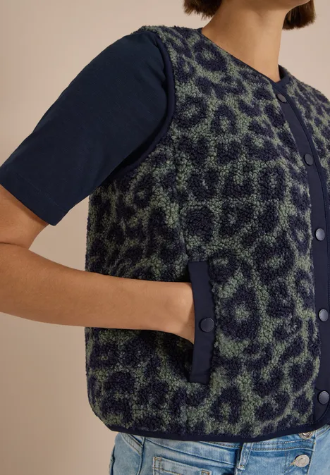 Teddy-Weste mit Softshelldetails und Leo-Muster dried olive green Eine Person trägt eine dunkelgrüne, leopardgemusterte Weste mit Knöpfen über einem marineblauen T-Shirt und Jeans.