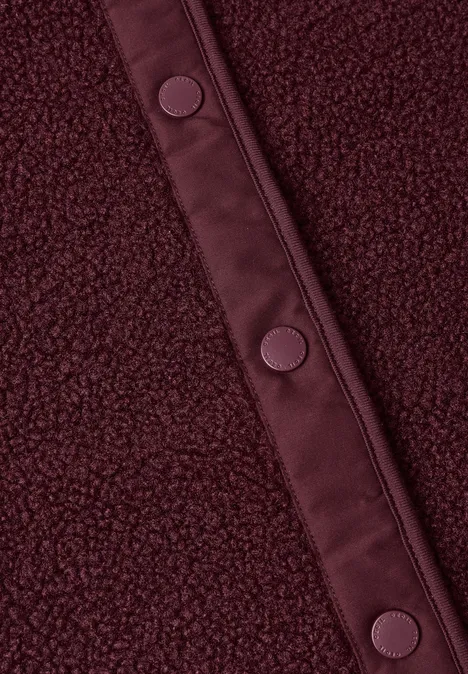 Teddy-Weste mit Softshelldetails red wine Nahaufnahme eines burgunderroten Fleece-Stoffes mit Ledereinfassung und Druckknöpfen.