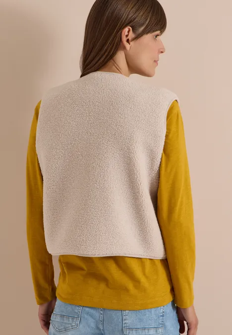 Femme de dos portant une veste sherpa crème sur un t-shirt à manches longues moutarde et un jean.