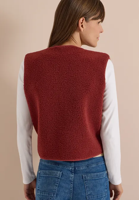 Person von hinten mit roter Fleece-Weste, weißem Langarmshirt und blauen Jeans.