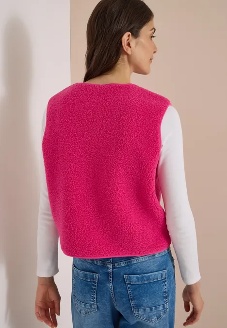 Kobieta widziana od tyłu w różowej, puszystej kamizelce, białym longsleeve i niebieskich dżinsach.