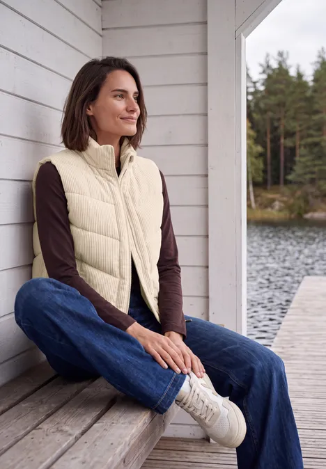 Cord-Weste mit Steppmuster und Zipper pearl beige Eine Frau sitzt entspannt auf einer Terrasse am See, trägt Jeans, Pullover und Steppweste.