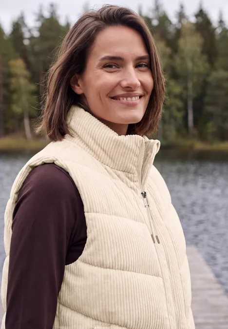 Cord-Weste mit Steppmuster und Zipper pearl beige Lächelnde Frau in beiger Weste steht an einem Steg vor Wasser und Wald.