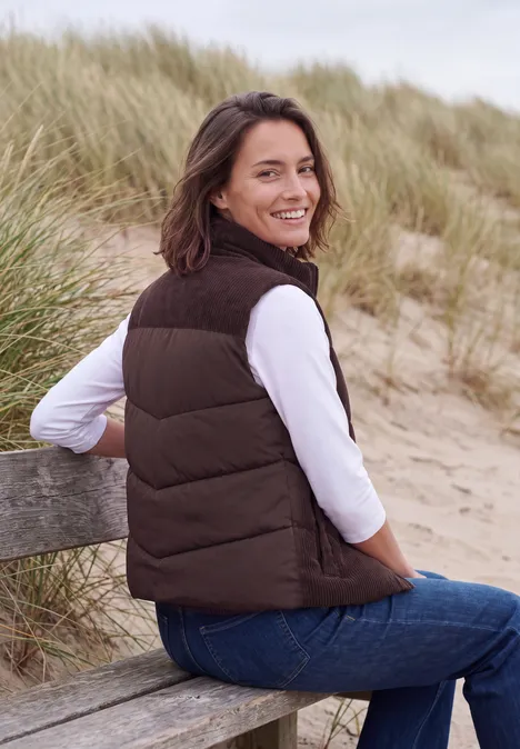 Corduroyvest met doorgestikt patroon en ritssluiting berry red Glimlachende vrouw in bruine bodywarmer zit op een bankje in de duinen