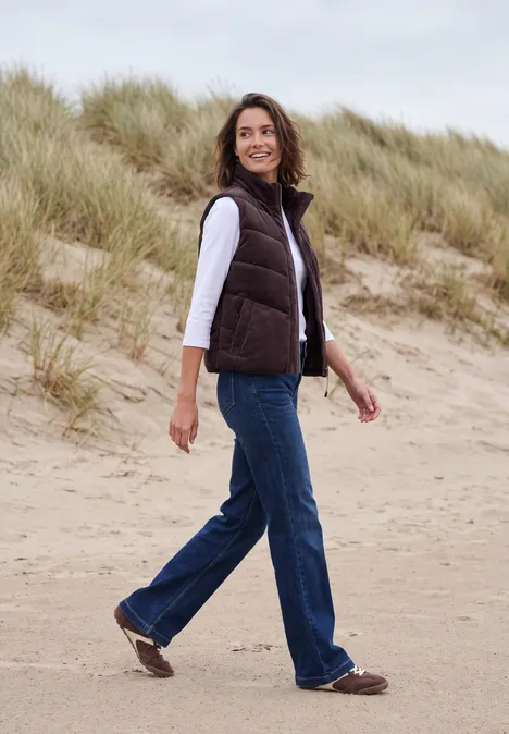 Corduroyvest met doorgestikt patroon en ritssluiting berry red Vrouw in casual outfit wandelt over het zandstrand met duinen en helmgras op de achtergrond.