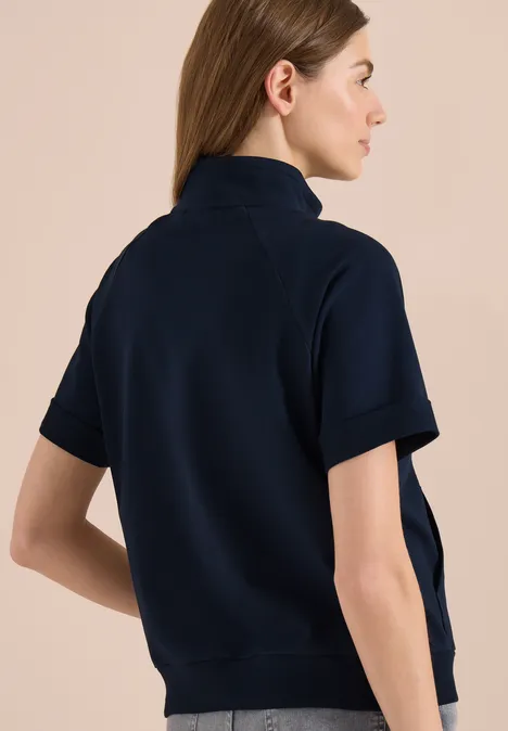 Vue de dos d’une personne portant un sweat-shirt à manches courtes et col montant bleu foncé.