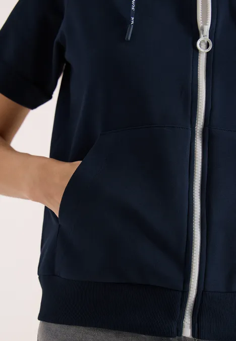 Une personne porte un sweat à capuche bleu marine à fermeture éclair et a la main dans la poche avant.