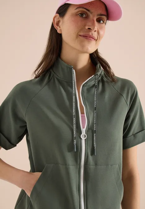 Person in olivgrüner, kurzärmliger Jacke mit Reißverschluss und Kängurutaschen.