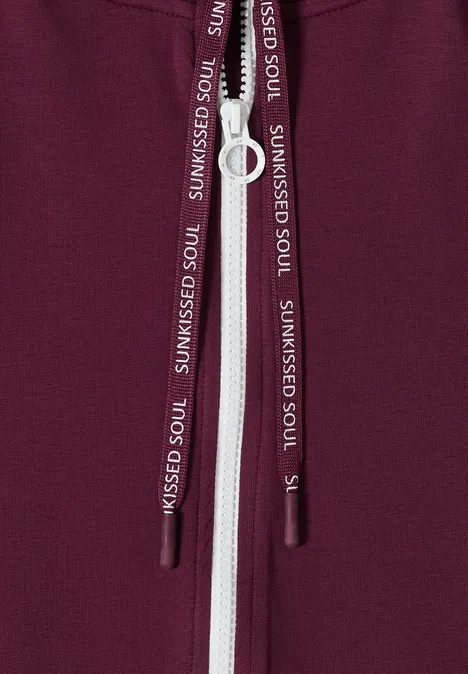 Nahaufnahme eines bordeauxfarbenen Hoodies mit weißem Reißverschluss und Kordeln mit Aufdruck SUNKISSED SOUL