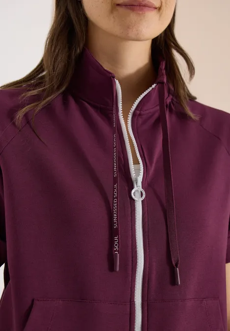 Bordeauxfarbene Damenjacke mit kurzem Arm, hohem Stehkragen, weißem Reißverschluss und schwarzen Kapuzenkordeln.