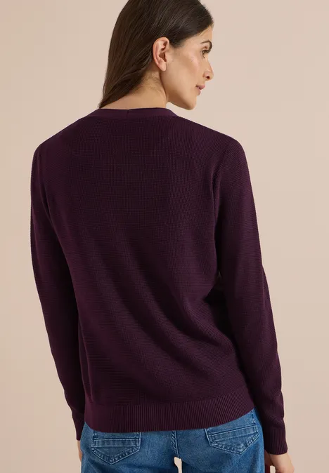Femme de dos portant un pull violet foncé et un jean bleu.