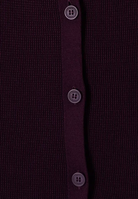 Gros plan sur un gilet en maille violet foncé, quatre boutons alignés verticalement.