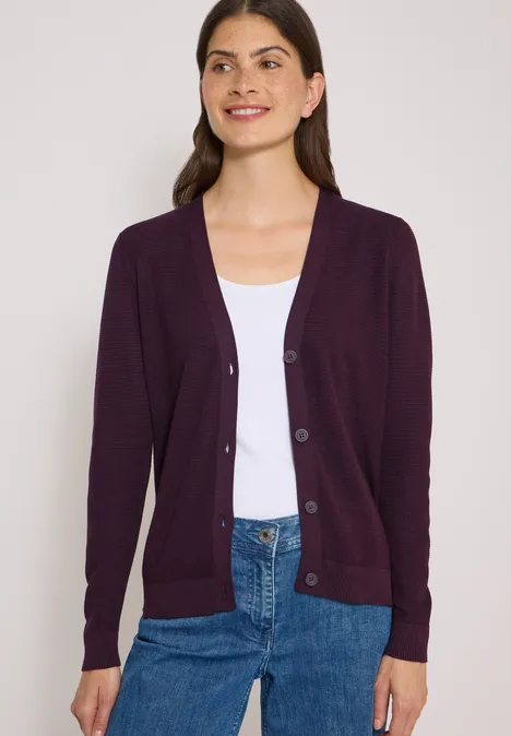 Femme portant un gilet violet sur un débardeur blanc et un jean bleu.