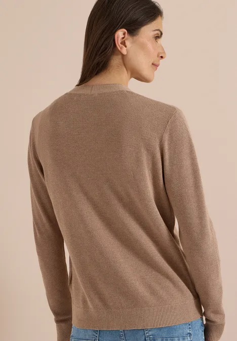 Femme de dos portant un pull marron à manches longues sur fond beige.