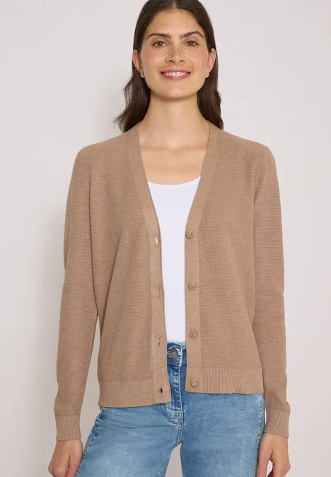 Femme porte un cardigan beige, un haut blanc et un jean