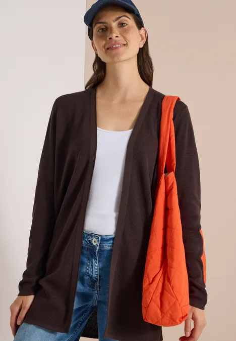 Femme en jean, débardeur blanc, gilet foncé, casquette bleue et sac orange