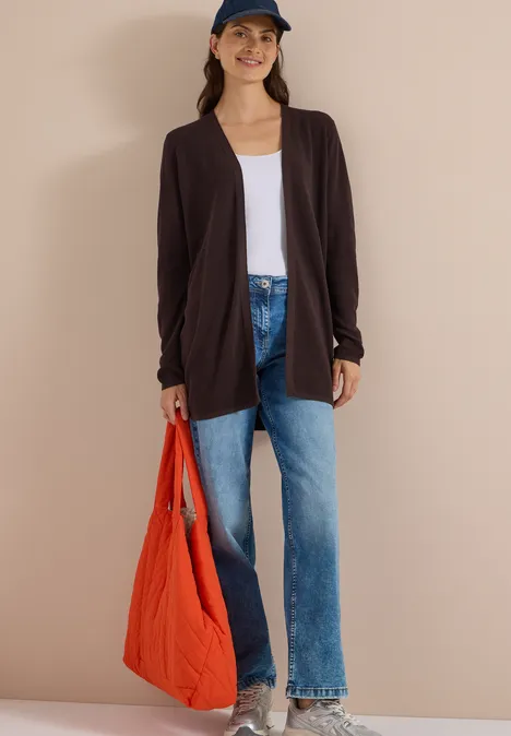 Femme en cardigan noir, t-shirt blanc, jean bleu, casquette et sac rouge sur fond beige.