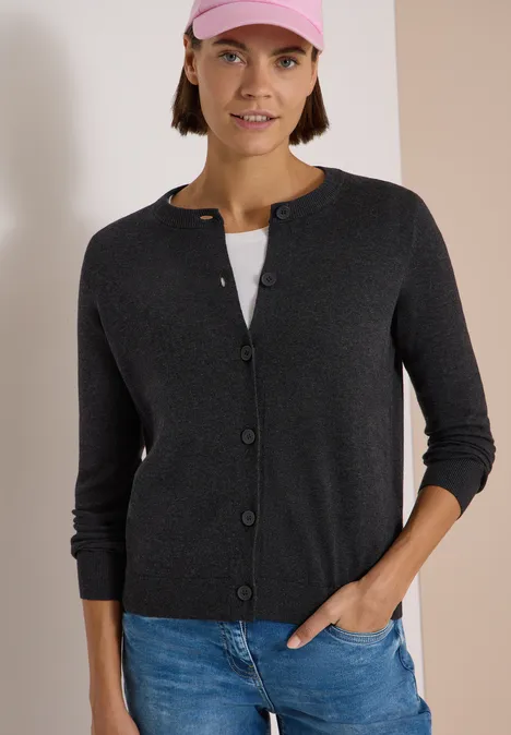 Cardigan boutonné à col rond charcoal grey melange Femme portant un gilet gris, jean et casquette rose devant un fond bicolore sobre.