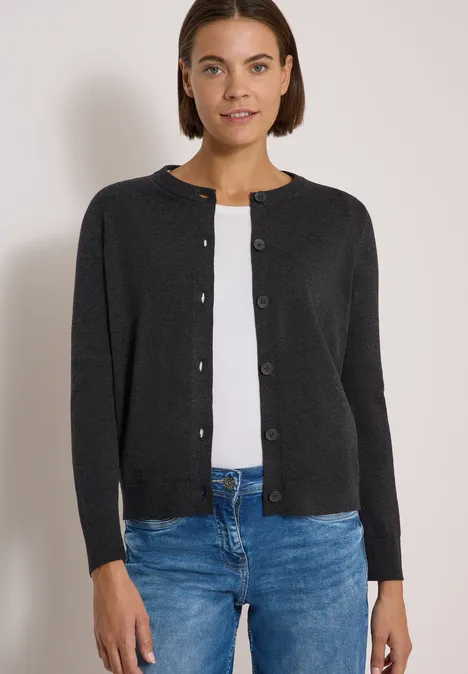 Cardigan boutonné à col rond charcoal grey melange Une femme porte un gilet noir à boutons sur un t-shirt blanc et un jean bleu.