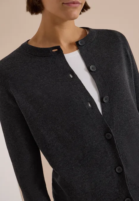Cardigan boutonné à col rond charcoal grey melange Un gilet gris foncé à boutons porté sur un top blanc.