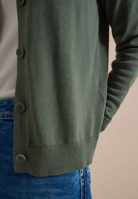 Eine Person trägt eine smaragdgrüne Strickjacke mit großen Knöpfen und Jeans.
