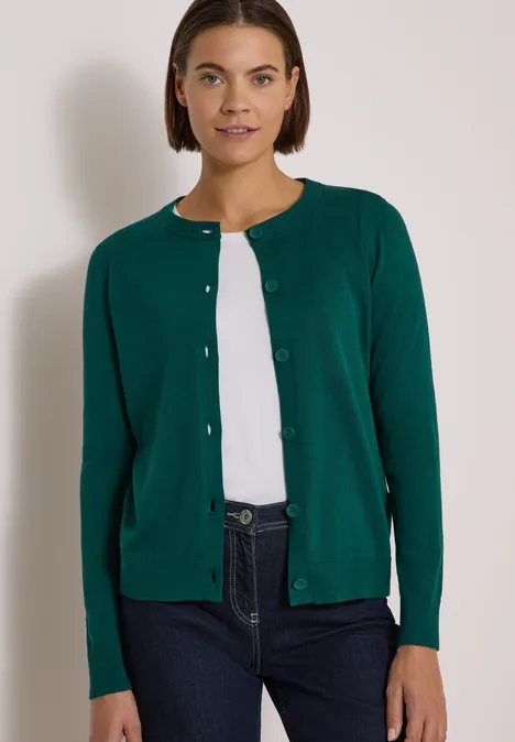 Cardigan boutonné à col rond dark fir green Femme porte un cardigan vert, un t-shirt blanc et un jean sur fond clair.