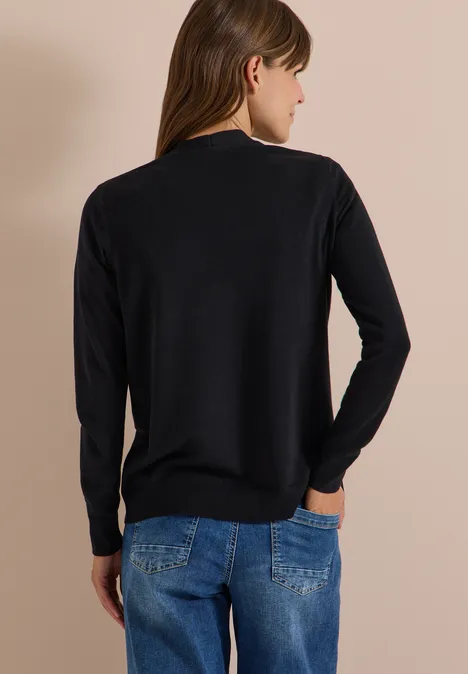 Vrouw van achteren in een zwarte trui en blauwe jeans voor een beige achtergrond.
