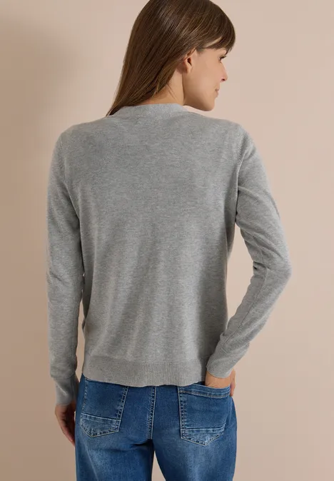 Cardigan boutonné à col V mineral grey melange Frau von hinten mit langem braunen Haar, grauem Langarmshirt und blauen Jeans vor hellem Hintergrund.