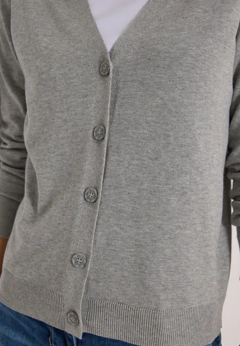 Cardigan boutonné à col V mineral grey melange Graue Strickjacke mit Knöpfen über weißem Shirt, kombiniert mit Jeans.
