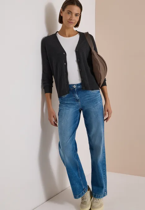 Cardigan boutonné à col V charcoal grey melange Une femme appuyée contre un mur clair porte un t-shirt blanc, un gilet noir et un jean bleu large.