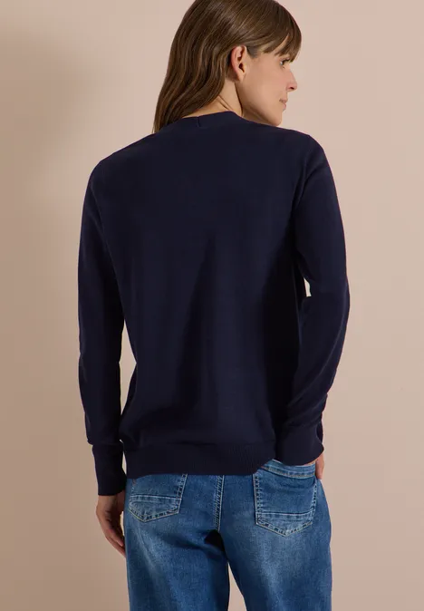 Vrouw van achteren in een marineblauwe trui en spijkerbroek voor een beige achtergrond.