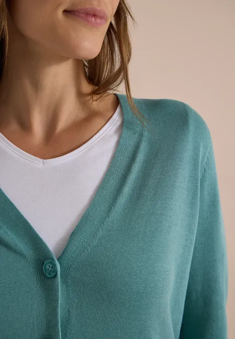 Een vrouw draagt een turquoise vest over een wit shirt.