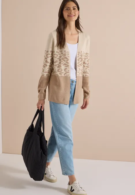Modell in beiger, Leo-Print-Strickjacke, weißem Top, hellblauen Jeans, weißen Sneakern und großer schwarzer Schultertasche.