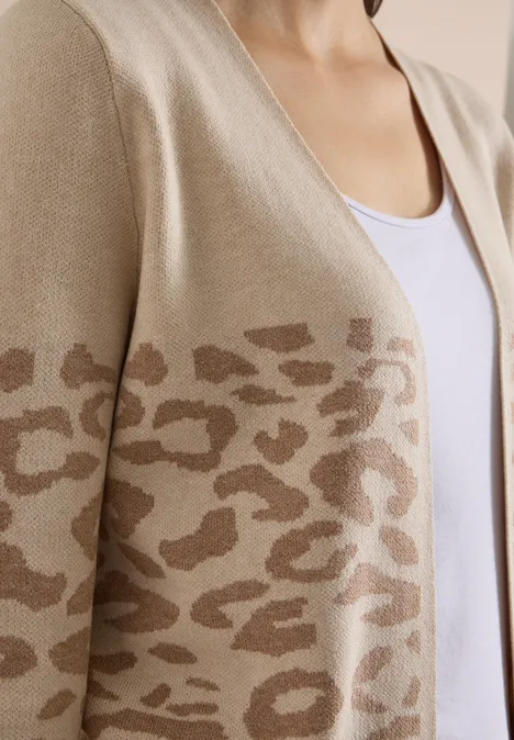 Eine Person trägt ein beiges Strickjäckchen mit braunem Leopardenmuster und einem weißen Top.