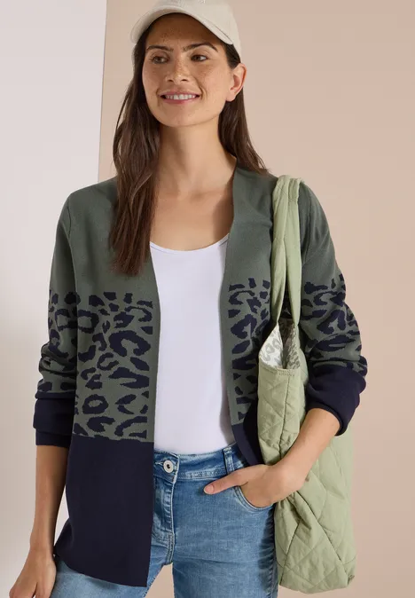 Frau in Cap, weißem Top, zweifarbigem Cardigan mit Leopardenprint, Jeans und gesteppte Tasche.