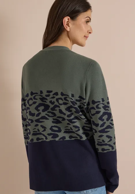 Frau mit dunklen Haaren von hinten, Pullover in Olivgrün mit Leopardenmuster und dunkelblauer unteren Partie.