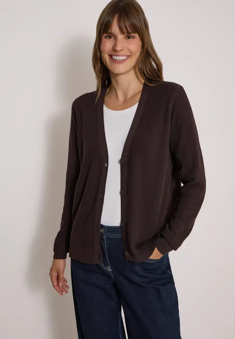 Kardigan z dekoltem w szpicu i strukturą truffle brown Uśmiechnięta kobieta ma na sobie ciemnobrązowy kardigan, biały t-shirt i niebieskie dżinsy.