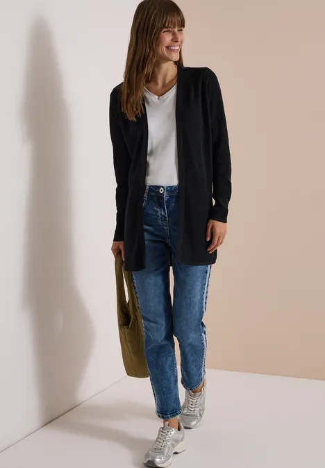 Open vest met lange mouwen Black Frau trägt schwarzen Cardigan, weißes V-Neck-Shirt, blaue Jeans, Sneakers und hält olivgrüne Tasche.