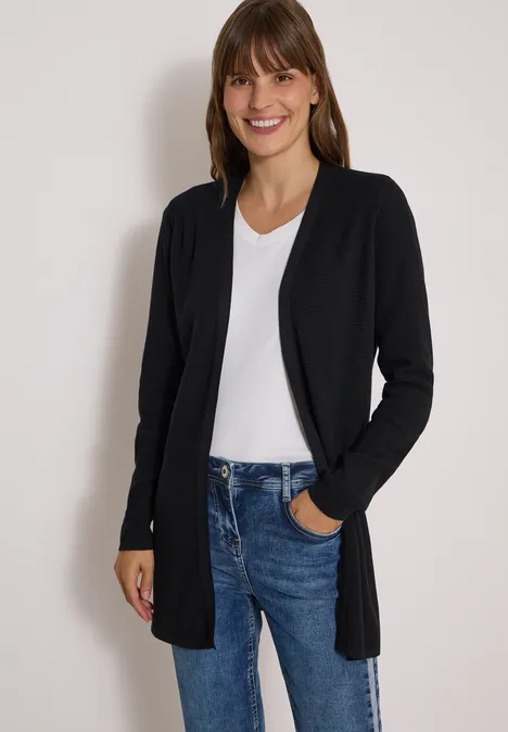 Open vest met lange mouwen Black Eine lächelnde Frau trägt eine schwarze Strickjacke, weiße Bluse und blaue Jeans.