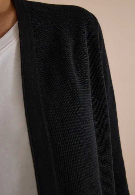 Open vest met lange mouwen Black Schwarz gestrickter Cardigan über weißem T-Shirt, nur Oberkörper sichtbar.