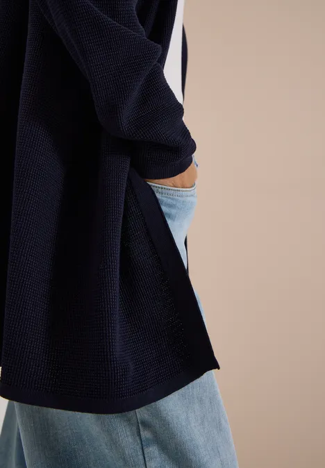 Open vest met lange mouwen urban dark blue Ein dunkelblauer Cardigan über weißem Top, kombiniert mit hellblauen Jeans und Hand in Hosentasche.