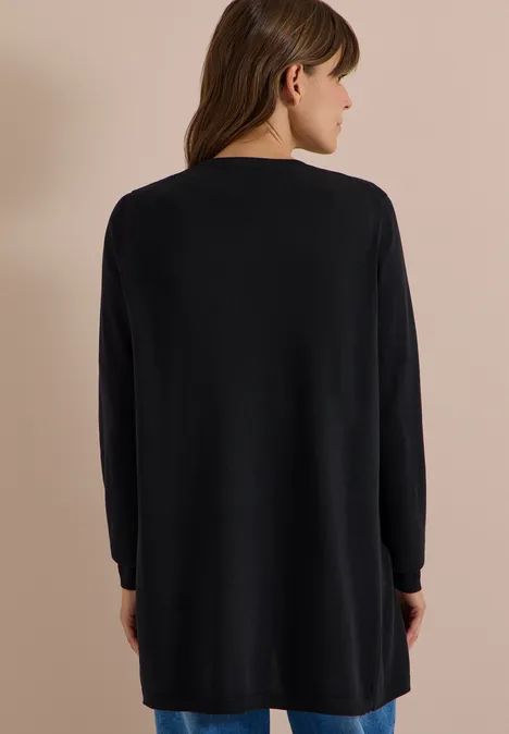 Een vrouw van achteren draagt een lange zwarte trui tegen een neutrale achtergrond.
