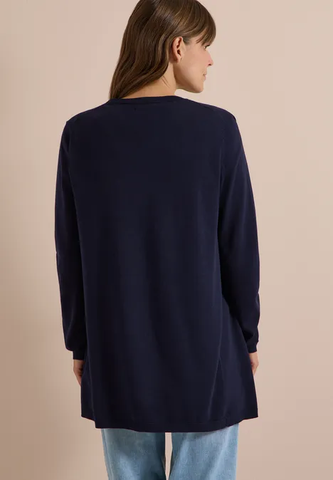 Vrouw van achteren in een losvallende donkerblauwe cardigan voor een lichte beige achtergrond.