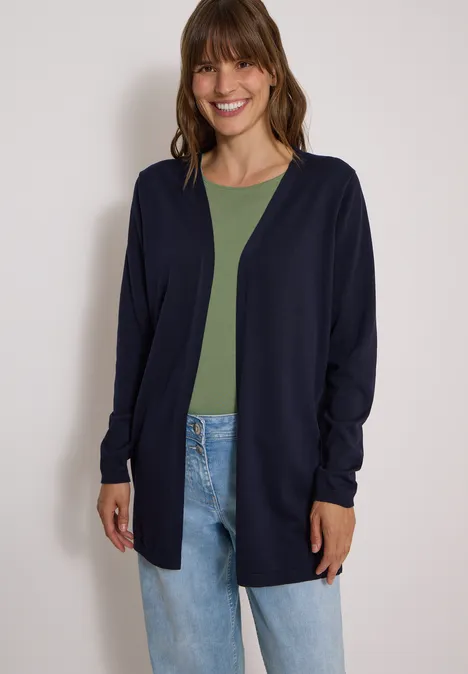 Vrouw lacht in een marineblauwe cardigan met groen shirt en spijkerbroek.